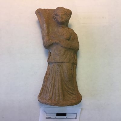 Figurine, single mold. Standing female musician in contrapposto pose, wearing peblos, diadem and double necklace, holds harp on right shoulder. Selucid, Parthian. Clay.; YPM BC 016826