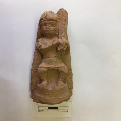 Figurine, single mold. Bow legged dwarf holding harp on right shoulder, wearing tall pointed cap and short kilt exposing genitals, ponytail by right ear. Standing on round pedestal. Old Babylonian. Clay.; YPM BC 016852