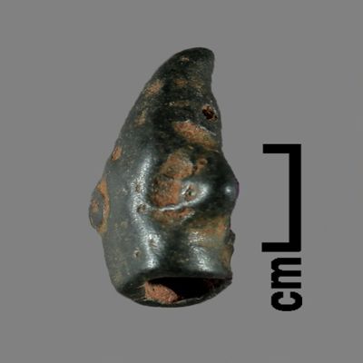 Figurine fragment. Head of anthropomorphic figure, hollow, conical hat slightly curved forward, hole under right eye. Bronze.; YPM BC 031155