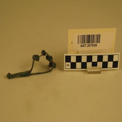 Woman's copper clothes pin. Specimen has central spine with 10 small rectangular tabs projecting from each edge. 7 of the tabs hold small copper replicas of pottery vessels. Tag attached to specimen identifies it as woman's fibula pin, 200 B.C. Length 3 1/2'. Antioch, Syria.; YPM ANT 207936