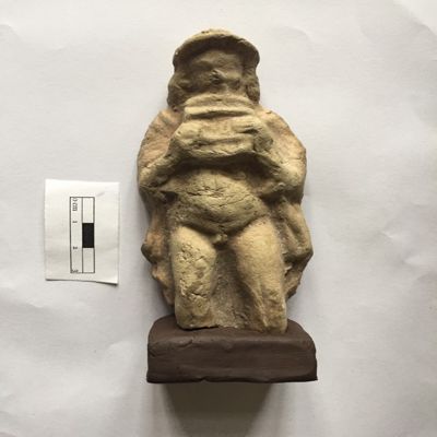 Figurine, single mold. Male musician in contrapposto pose, holding syrinx (panflute) in both hands, wearing flat rounded cap, flowing drape covers shoulders and arms, exposed front. Long hair falls to shoulders. Selucid, Parthian. Clay.; YPM BC 016862